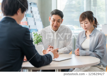 一對夫婦在聆聽，一位商人在陳列室/商務談判空間為客戶提供服務 123629427