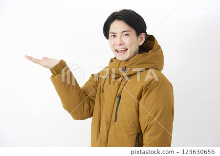 一名身穿羽絨外套的男子用手掌指向白色背景下的左側 123630656