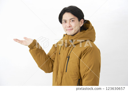 A man wearing a down jacket points to the left with his palm on a white background A man wearing a down jacket points to the left with his palm on a white background 123630657