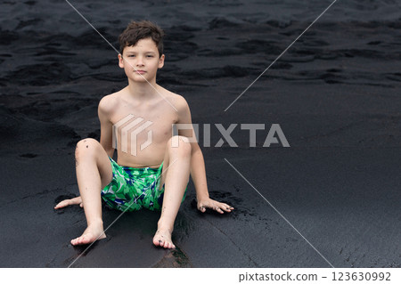 Teen boy is sitting on the Black sand beach in Hawaii. 123630992
