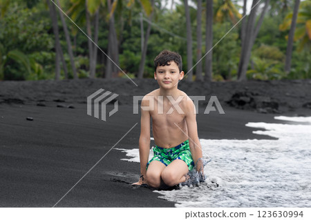 Teen boy is sitting on the Black sand beach in Hawaii. 123630994