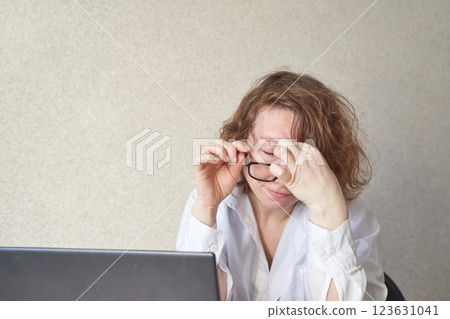 Caucasian mature female struggling with eyeglasses at laptop in office setting Caucasian mature female struggling with eyeglasses at laptop in office setting 123631041