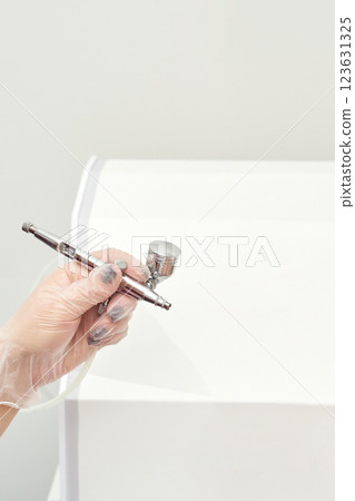 Close up of hand holding airbrush in gloved hand against minimalist white Close up of hand holding airbrush in gloved hand against minimalist white 123631325