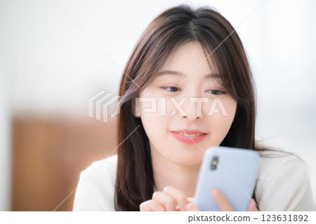 特寫：一位年輕女子麵朝下躺在房間裡，看著自己的智慧型手機 123631892