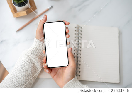 A close up of the pair of hand holding blank screen smartphone over an open notebook on the table. 123633736