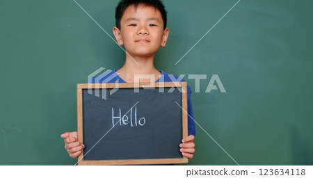 Front view of Asian schoolboy writing and showing text on slate chalkboard in classroom at school 123634118