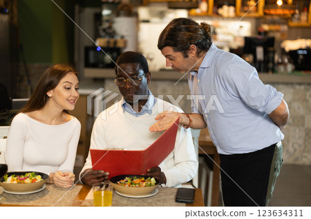 Waiter helping couple choose food and wine at restaurant Waiter helping couple choose food and wine at restaurant 123634311