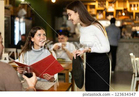 Girl waiter communicates with female customer, serve couple in restaurant Girl waiter communicates with female customer, serve couple in restaurant 123634347