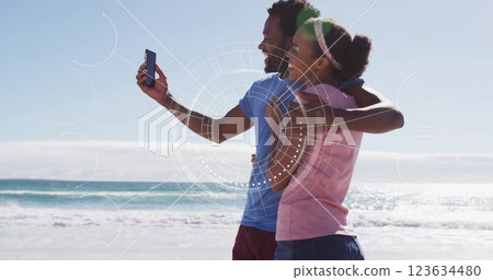 Couple on beach with smartphone, digital interface image over them Couple on beach with smartphone, digital interface image over them 123634480