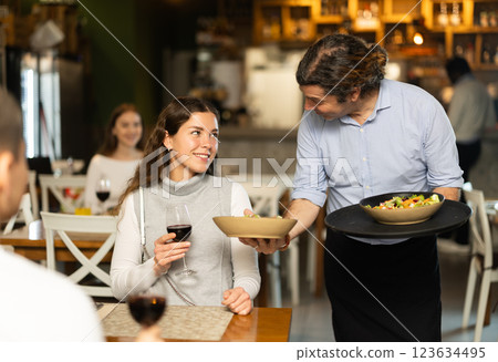 Man waiter serves cafe establishments girl visitor, puts food on table. 123634495