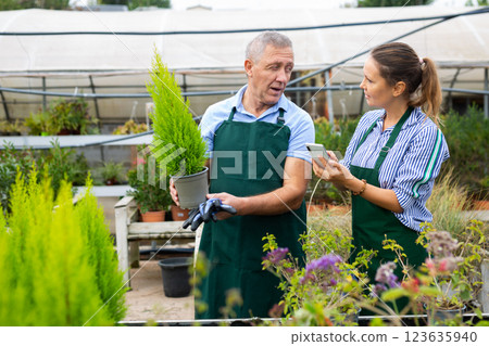 Positive man and woman in uniform taking photo of name of plant on smartphone in conservatory Positive man and woman in uniform taking photo of name of plant on smartphone in conservatory 123635940