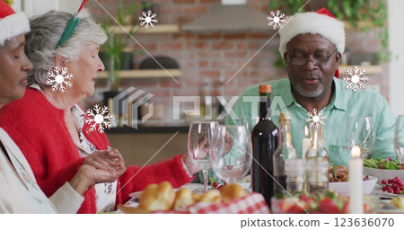 Image of white snowflakes over diverse senior friends in hats saying grace at christmas dinner Image of white snowflakes over diverse senior friends in hats saying grace at christmas dinner 123636070