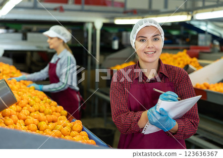 Young female supervisor with papers inspecting mandarins sorting workshop 123636367