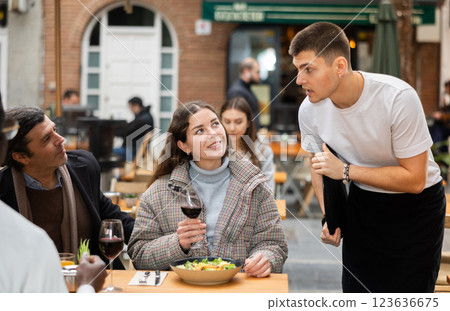 On open area of cafe, guy waiter communicates with couple of customer, accepts order 123636675