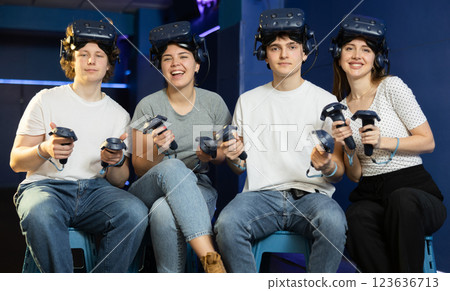 four smiling students with virtual reality devices sit and pose in gaming modern club four smiling students with virtual reality devices sit and pose in gaming modern club 123636713