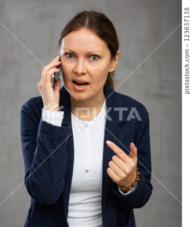 Indignant adult woman in jacket talking on phone 123637138