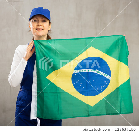 Smiling adult woman in uniform holding flag of Brazil Smiling adult woman in uniform holding flag of Brazil 123637196