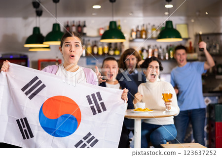 Excited young adult sports fans rooting for favorite team and waving flag of South Korea while watching match together in pub 123637252