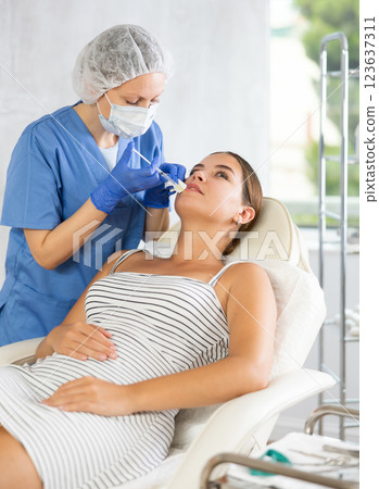 Adult woman cosmetologist makes injection in lips of patient Adult woman cosmetologist makes injection in lips of patient 123637311