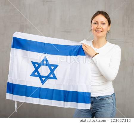 Happy young woman holding flag of Israel against unicoloured background 123637313