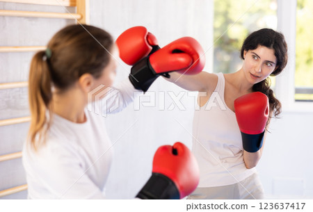 Focused woman practicing boxing punches in sparring during group self defence course Focused woman practicing boxing punches in sparring during group self defence course 123637417
