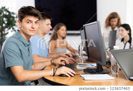Among students of computer academy programmers, young guy is sitting and smiling, looking away 123637463