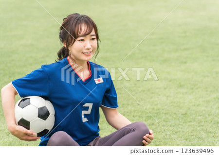 A woman in a soccer uniform sitting on a grass field with a soccer ball A woman in a soccer uniform sitting on a grass field with a soccer ball 123639496