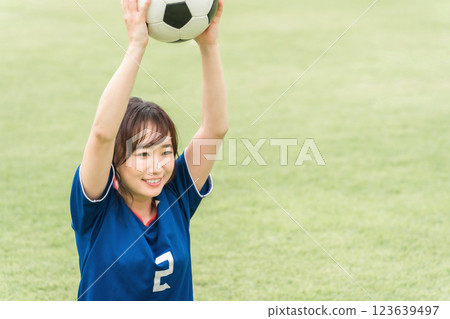 一名身穿足球服的女子坐在草地上，手裡拿著足球 123639497