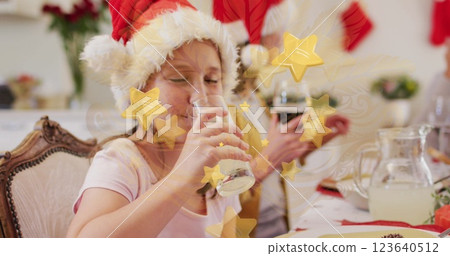 Image of carnival mask and stars over caucasian family with santa hats having christmas dinner Image of carnival mask and stars over caucasian family with santa hats having christmas dinner 123640512