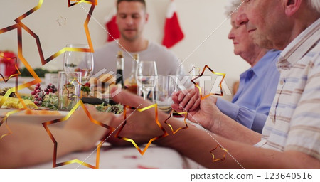 Image of stars over caucasian family with santa hats praying before christmas dinner 123640516