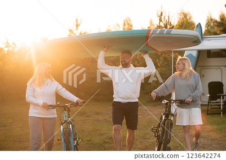 Friends enjoy a sunset adventure by the lake with bicycles and a paddleboard during an outdoor gathering Friends enjoy a sunset adventure by the lake with bicycles and a paddleboard during an outdoor gathering 123642274
