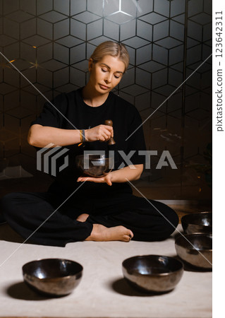 Practitioner uses singing bowls for meditation in a serene studio environment during a mindful evening session Practitioner uses singing bowls for meditation in a serene studio environment during a mindful evening session 123642311