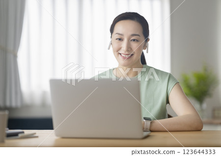 A woman in her 30s wearing earphones and facing a laptop computer, telework, online call image A woman in her 30s wearing earphones and facing a laptop computer, telework, online call image 123644333