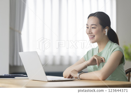 一位 30 多歲女性戴著耳機，面對著筆記型電腦，遠端辦公，線上通話圖片 123644371