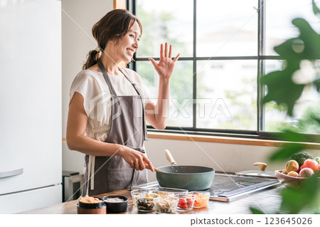 一個穿著圍裙的女人在廚房裡用煎鍋(微笑並揮手) 一個穿著圍裙的女人在廚房裡用煎鍋(微笑並揮手) 123645026