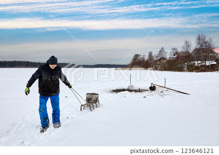 From frozen lake, farmer performs sapropel mining, using pole to scoop up organic matter through ice, gunk is moved by sleigh for soil enrichment during winter months in agriculture. 123646121