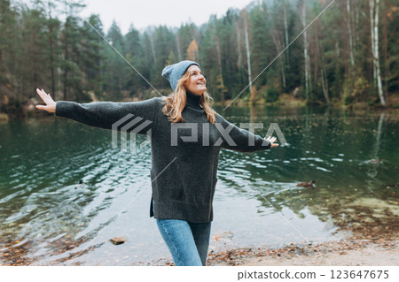 Happy woman raising hands up on the banks of the lake. Young 30s woman hiker in front smiling happy, hiking in woods, warm autumn day. Happy woman raising hands up on the banks of the lake. Young 30s woman hiker in front smiling happy, hiking in woods, warm autumn day. 123647675