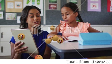 Image of emoji icons over biracial schoolgirl and teacher using tablet Image of emoji icons over biracial schoolgirl and teacher using tablet 123648399