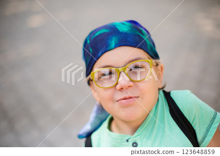 A funny little boy in glasses and a bandana, wearing a green t-shirt and denim shorts, having fun and joking 123648859