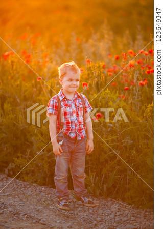 A funny young boy with eye misalignment, smiling and giggling in a sunset-lit poppy field 123649347