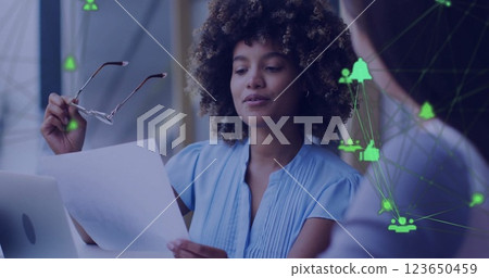 Image of network of connections with icons over diverse colleagues discussing work in office 123650459