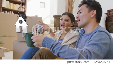 Image of silver house key and key fob over happy biracial couple by cardboard boxes 123650764
