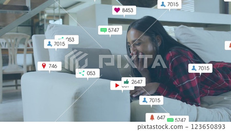 Image of media icons over biracial woman using laptop on couch 123650893