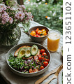 Fresh salad with tomatoes, avocado, and bread on table with flowers and juice. vibrant and healthy meal surrounded by nature beauty 123651102