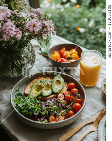 Fresh salad with tomatoes, avocado, and bread on table with flowers and juice. vibrant and healthy meal surrounded by nature beauty 123651102