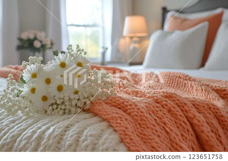 A bouquet of white daisies and baby's breath on a cozy bed with a knitted blanket in soft peach and white tones 123651758