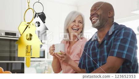Image of gold house key over diverse couple smiling in kitchen 123652353