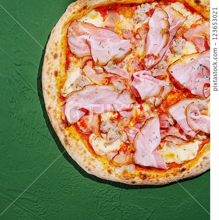 Delicious pizza topped with ham and cheese on green background Delicious pizza topped with ham and cheese on green background 123653021