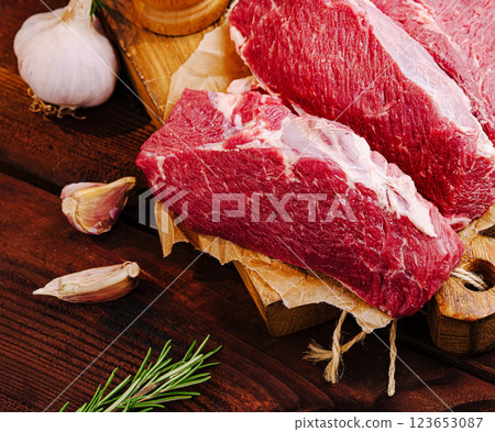 Fresh cuts of beef displayed with garlic and herbs on wooden board Fresh cuts of beef displayed with garlic and herbs on wooden board 123653087