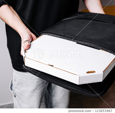Delivery worker presents a pizza box in a black bag 123653467